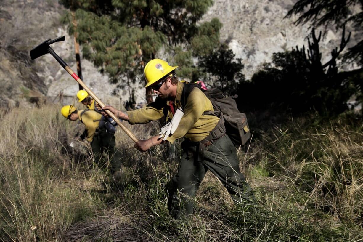 Firefighters clear brush as they battle the Colby Fire on Friday near Azusa, Calif.