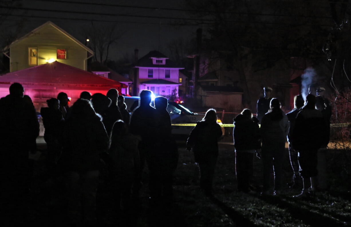 A crowd gathers in an alley east of Terrance Ave. South in west Columbus, Ohio where multiple shootings occurred Monday. A man shot and killed a couple and their 7-year-old son and wounded their 12-year-old daughter in a home Monday before being shot and killed by police responding to the scene, Columbus police said.