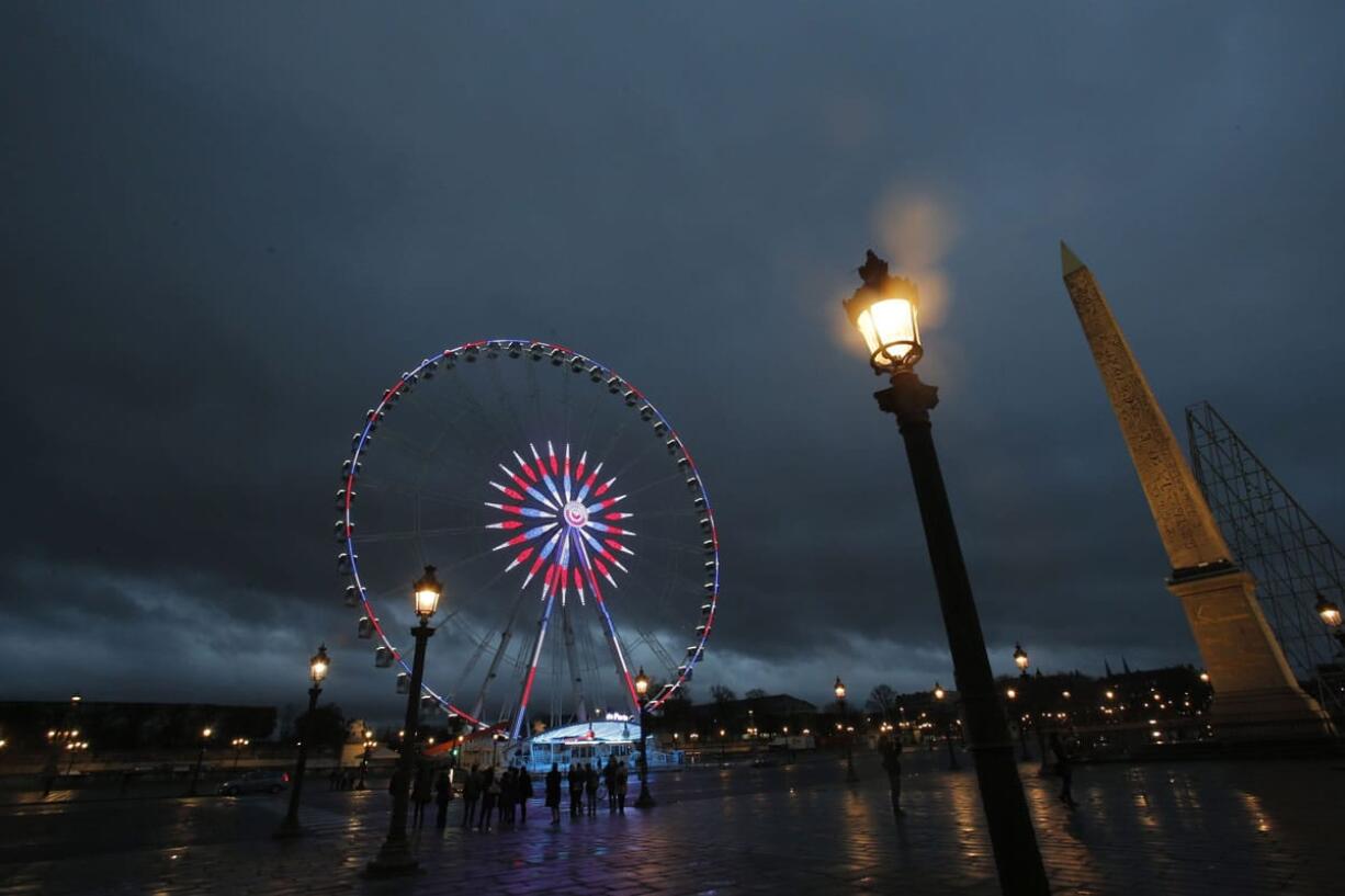 People gather near the ferris wheel illuminated with the French colors on the Concorde square in Paris on Tuesday. France invoked a never-before-used European Union &quot;mutual-defense clause&quot; to demand Tuesday that its partners provide support for its operations against the Islamic State group in Syria and Iraq and other security missions in the wake of the Paris attacks.