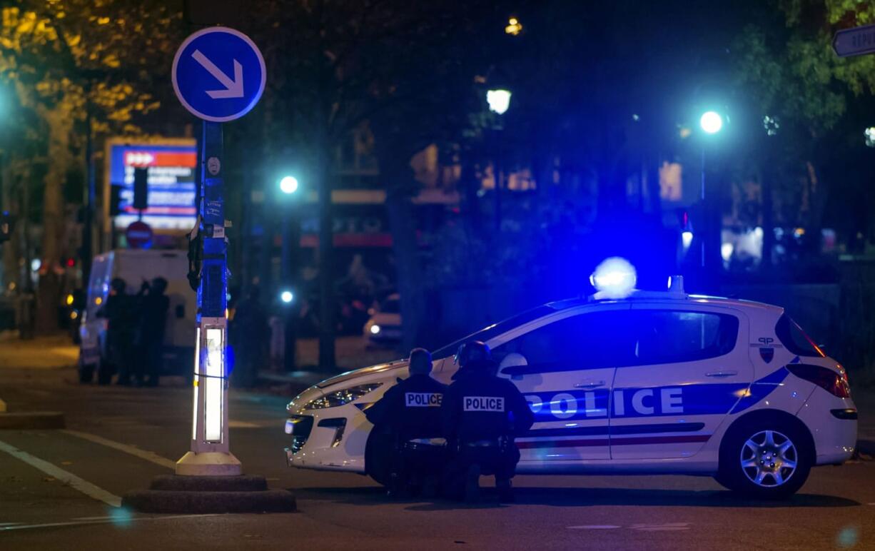 Police officers take cover behind a car outside the Bataclan theater in Paris.