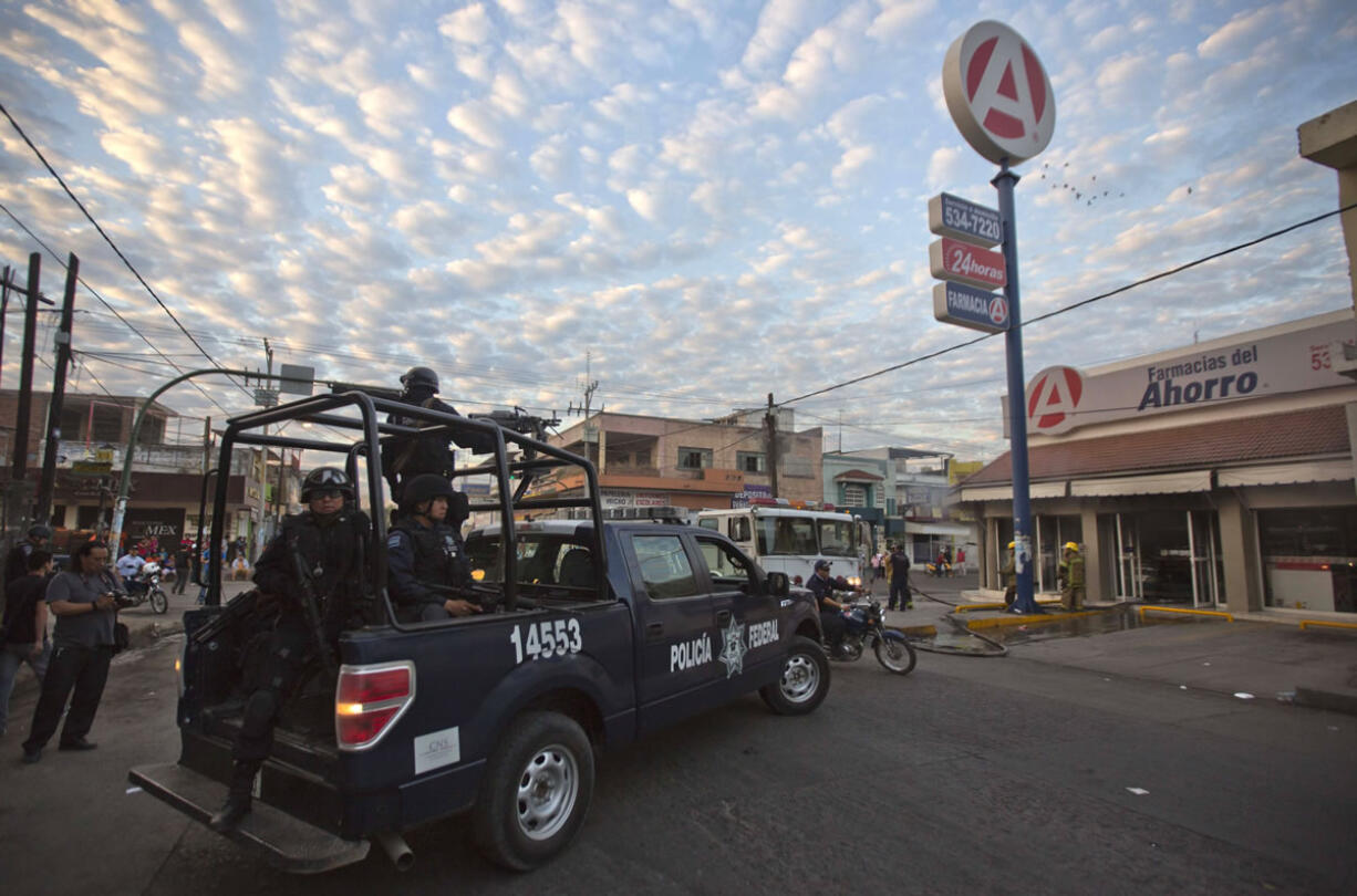 Federal police arrive Wednesday at a burned pharmacy in Apatzingan, Mexico, but drug cartels appeared to be carrying out business as usual.