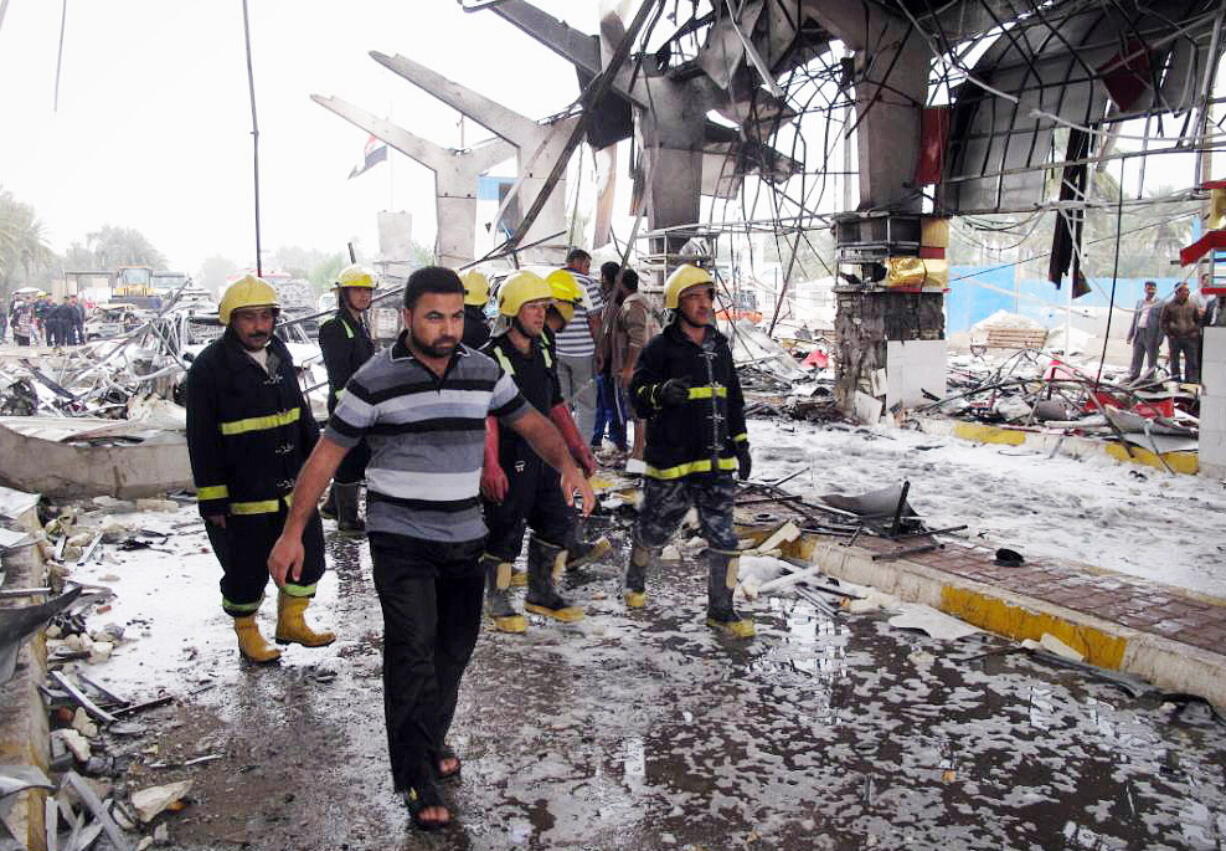 Firefighters and civilians inspect the site of a massive bomb attack in Hillah, about 60 miles south of Baghdad on Sunday.