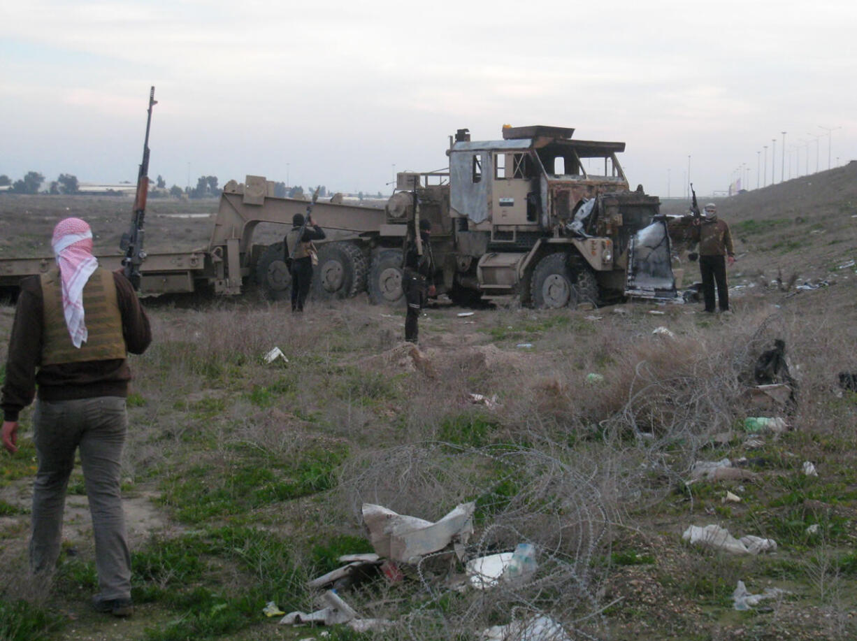 Gunmen inspect a damaged ammunition truck belonging to the Iraqi army Sunday after clashes with Iraqi security forces outside Fallujah, 40 miles west of Baghdad, Iraq.