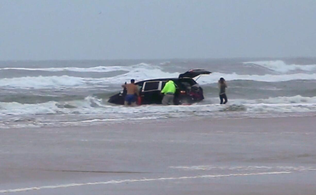 In this image from video, lifeguards and bystanders rescue three children Tuesday from a minivan in the surf at Daytona Beach, Fla.