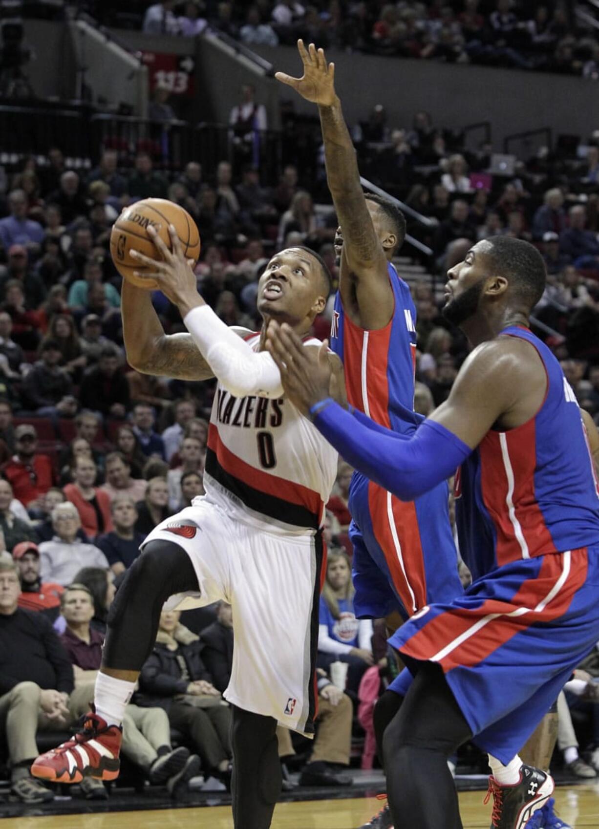 Portland Trail Blazers guard Damian Lillard, left, goes to the basket against the Detroit Pistons' Andre Drummond, right, and Brandon Jennings during the second half Monday.