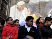 Students sit beneath an image of Pope Francis during a ceremony dedicating the City of Philadelphia Mural Arts Program?s mural, titled The Sacred Now: Faith and Family in the 21st Century on Monday in Philadelphia.(AP Photo/Matt Rourke)