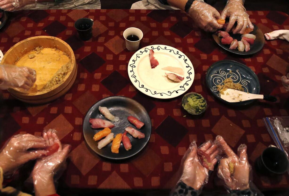 Tourists learn to make nigiri sushi with rice, top left, and slices of fish, as they prepare dinner at the home of Shino Fukuyama in Tokyo.