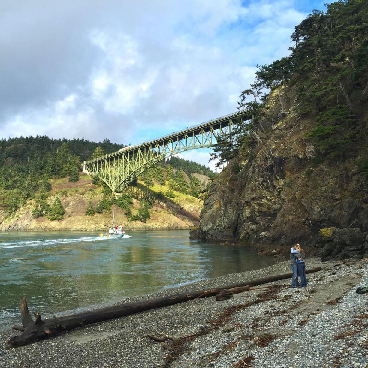 A couple embraces on North Beach with Deception Pass Bridge as a backdrop in Deception Pass State Park on Whidbey Island. Deception Pass, about 80 miles from Seattle, is the name of the strait that divides Washington&#039;s Whidbey Island from Fidalgo Island.