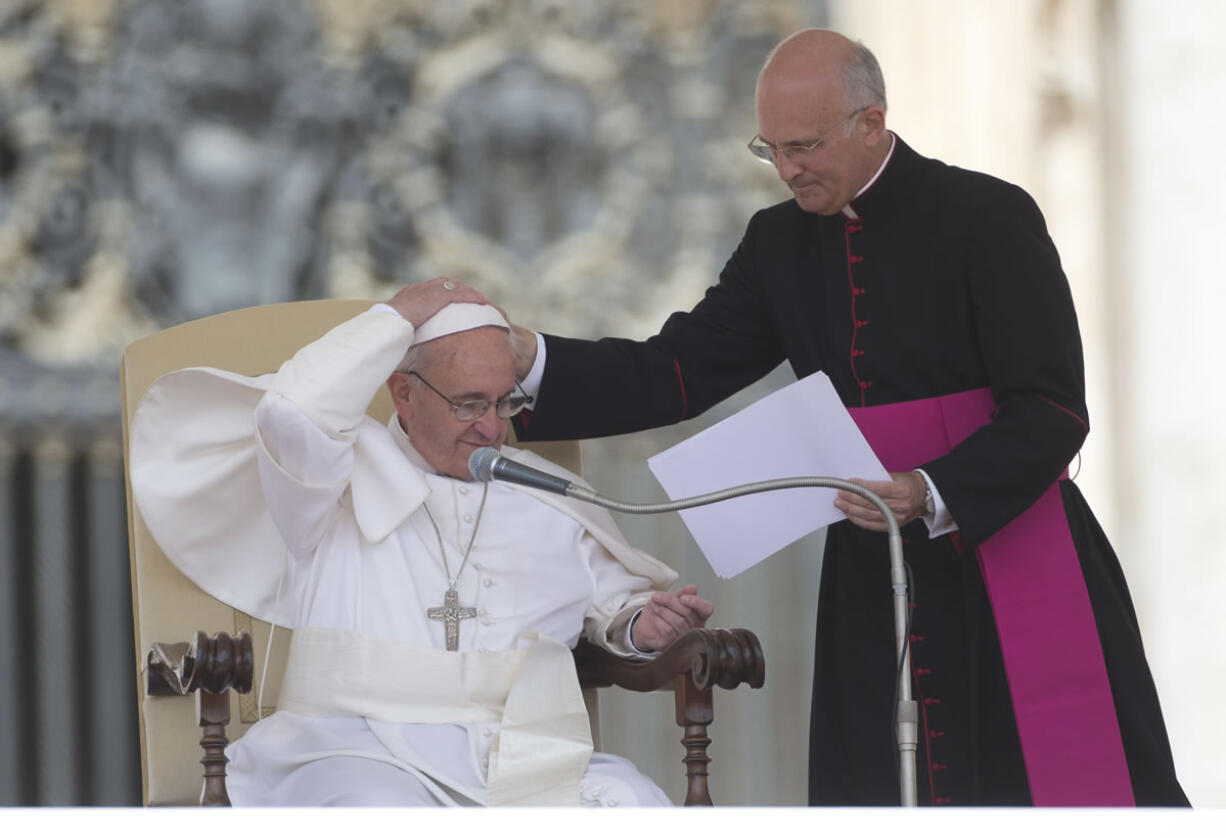 Pope Francis is helped by his personal secretary Mons. Alfred Xuereb, right, with his skull cap during a gust of wind while he attends his weekly open-air general audience in St. Peter's Square at the Vatican in May.