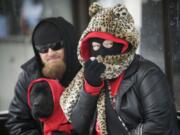 Trisha Pogue, right, covers her face from the cold while waiting for a city bus with Joshua Romine, left, and their dog Leah Friday morning in Vancouver.