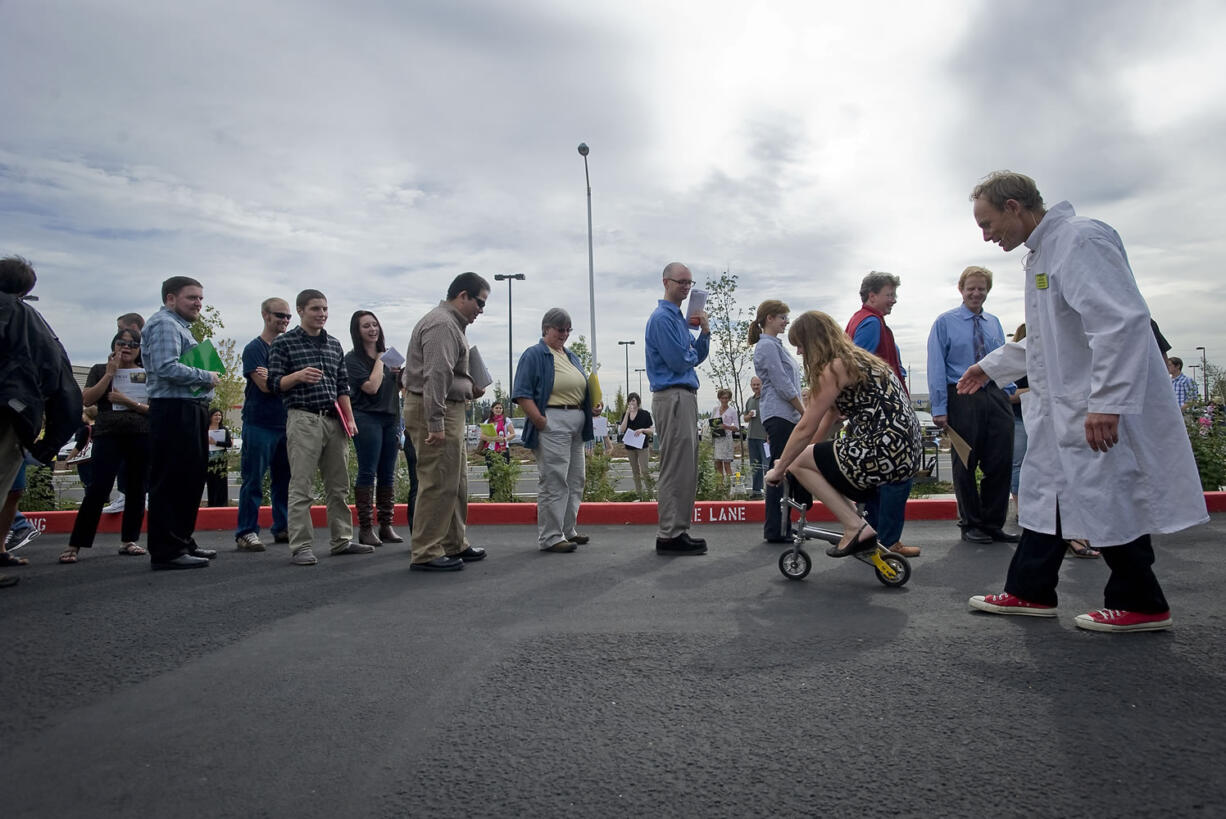 Mary Handy of Washougal takes a dare to ride a mini bicycle from Henrik Bothe, right, who was hired to keep a the crowd entertained at a New Seasons job fair at Life Point Church in September. Handy, who moved to the area from Idaho to be closer to family, quit her job at a convenience store when she moved two months ago and has been looking for a new job.