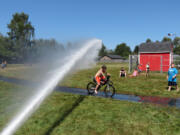 As temperatures reached toward 100 degrees today, children gathered at Hamllik Park on Addy Street in Washougal to cool off beneath the spray of the Camas and Washougal Fire Department fire hose. Children can get drenched at the park again tomorrow, from 11 a.m.