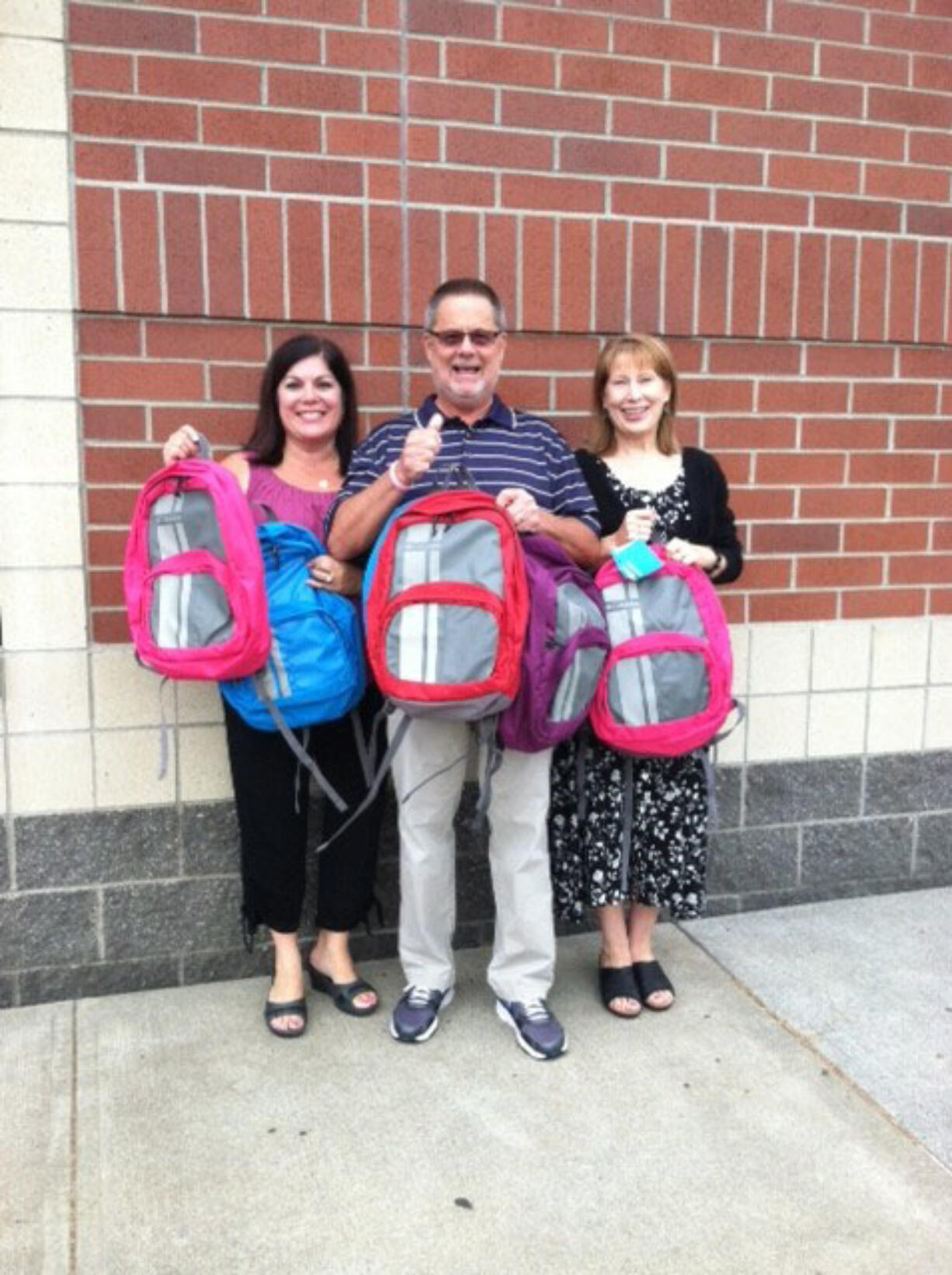 From left, principals Laura Bolt, Rex Larson and Mary Lou Woody display backpacks their schools received, filled with supplies, for children in need.