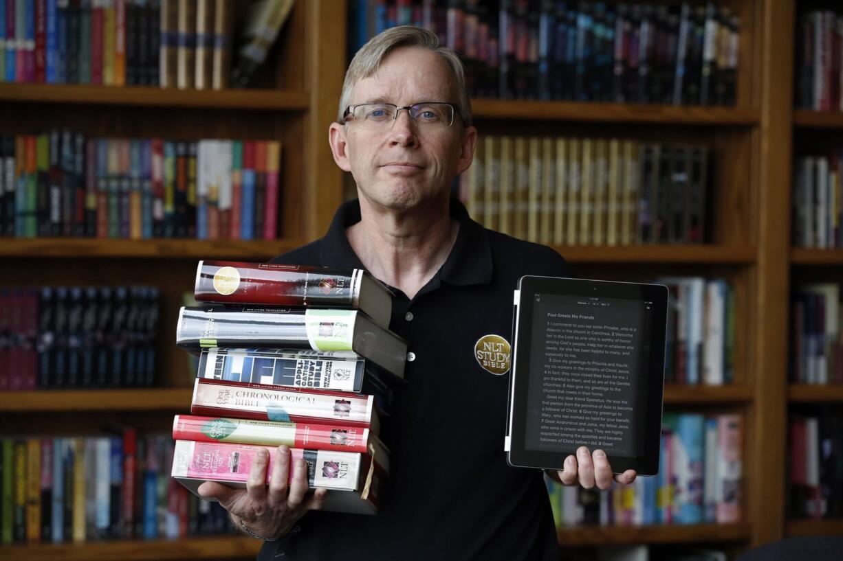 Jeffrey Smith, New Living Translation brand director at Tyndale House Publishers, holds some of the different editions of the New Living Bible used in the free YouVersion app, opened on his iPad in Carol Stream, Ill.