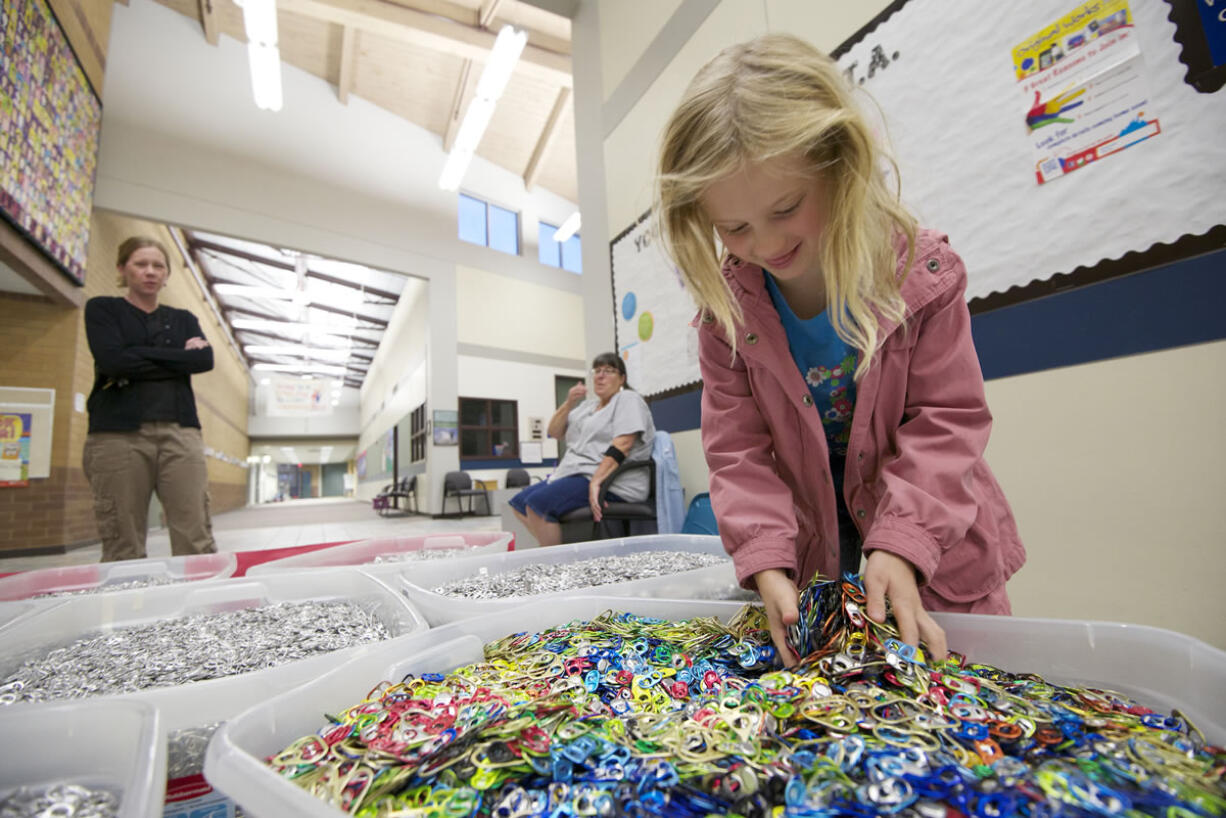 Lila Sloan, 6, a student at Lake Shore Elementary School, sifts through pull tabs as her mom, Lara, left, watches Monday in Vancouver.