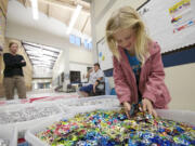 Lila Sloan, 6, a student at Lake Shore Elementary School, sifts through pull tabs as her mom, Lara, left, watches Monday in Vancouver.