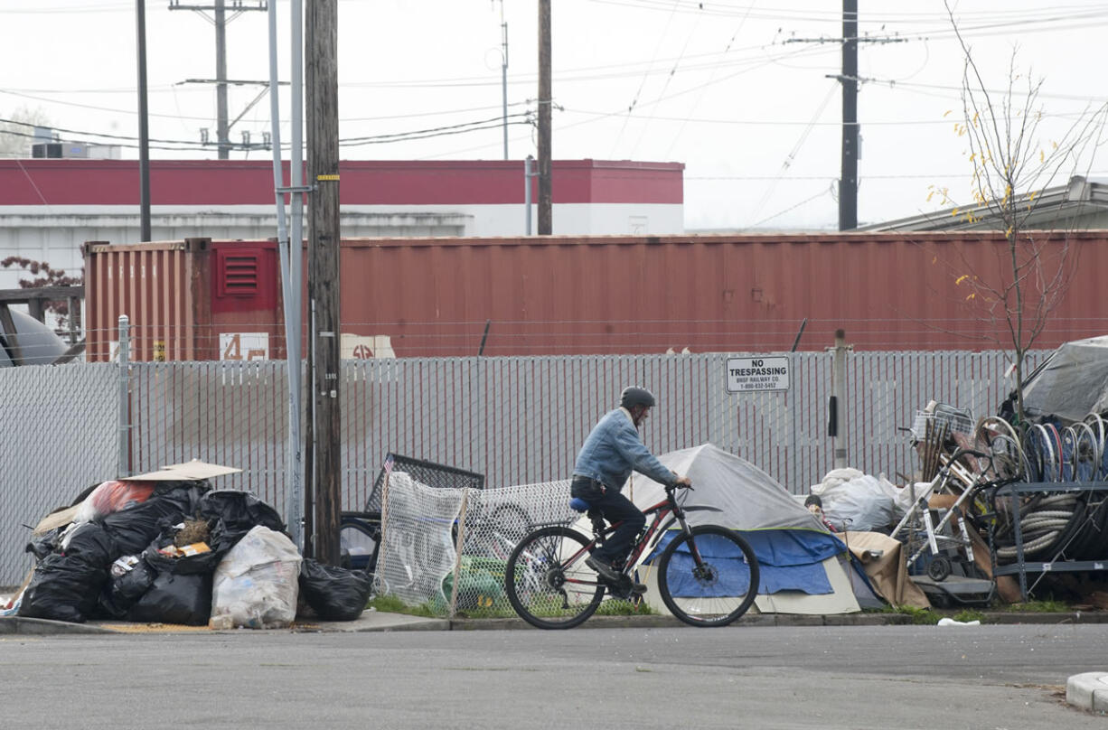 Oct. 21: A man cycles on a street next to a large pile of garbage and tents where homeless people used to live near Share House in downtown Vancouver.