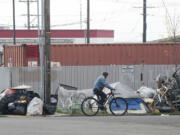 Oct. 21: A man cycles on a street next to a large pile of garbage and tents where homeless people used to live near Share House in downtown Vancouver.