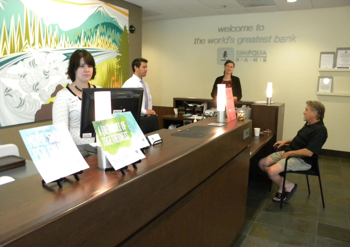 Associates Rebecca Glose, from left, and Derrick Luiz; manager Naomi Camargo; and customer Marty Hill do business Friday at the Umpqua Bank branch near Esther Short Park in Vancouver.