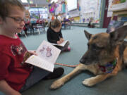 Harry Eddington shows therapy dog Raika a picture while reading out loud with classmate Britni Stapleton, background, in Andrea Edwards' first-grade classroom at Woodland Primary School.