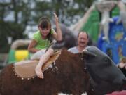 Talayna Dunaway, 7, of Battle Ground, does her best to stay atop a mechanical bull while her grandfather David Green watches from the background at Harvest Days in Battle Ground on Sunday July 22, 2012.