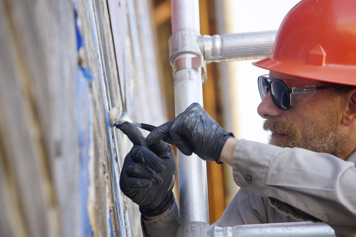 Cary Porter, a maintenance worker at Fort Vancouver National Historic Site, uses a spoon as a tool for smoothing sealant Friday as part of a re-chinking project at the  two-story fur store.