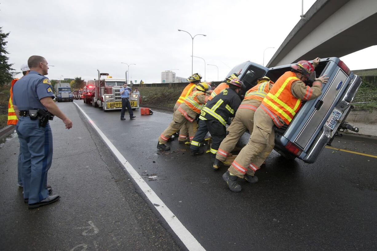 Washington State Patrol Sgt. Joel Gordon watches as Vancouver firefighters push a truck upright at the scene of a rollover accident on the ramp to state Highway 14 from northbound Interstate 5 shortly after 3 p.m.