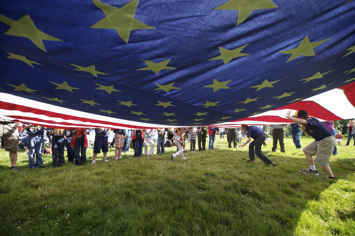 Cub Scouts, Boy Scouts, Girl Scouts and National Park Service staff members display a large flag during the Pledge of Allegiance at the annual Flag Day ceremony Thursday at the Parade Ground.