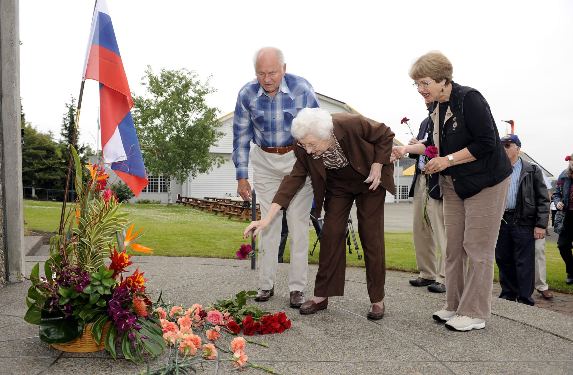 Former State Rep. Val Ogden, center, with Robert Buker, left, and Gayle Rothrock, place flowers at the Transpolar Flight Monument on Wednesday.