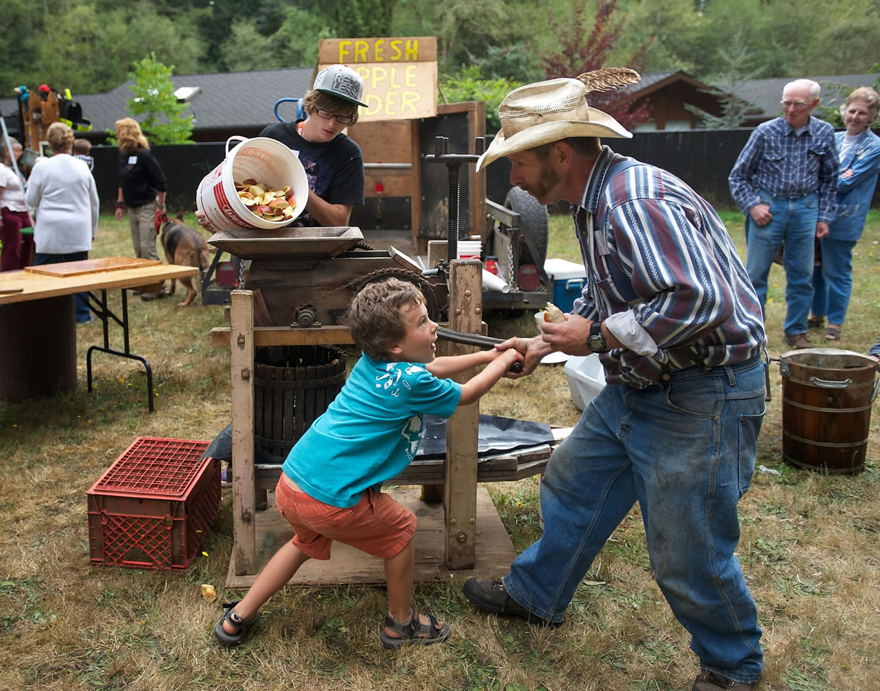 Rowan Rippl, 7, of La Center, works the apple cider press with help from JR Robertson, right, of Vancouver and volunteer Glen Montanye, back, 16, of Venersborg, during Homestead Day at the historic Venersborg Schoolhouse on Sunday.