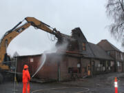 Battle Ground: Kyle Crawford of 3 Kings Environmental Inc. keeps dust down with water as the 1935 Battle Ground School District bus barn and home economics building is demolished Dec.