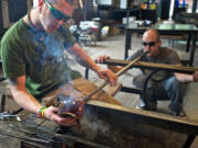 Andrew Lueck, manager of Firehouse Glass Studio, smooths and shapes the glass with newspaper while the shop tech Josh Handcock blows through the pipe.