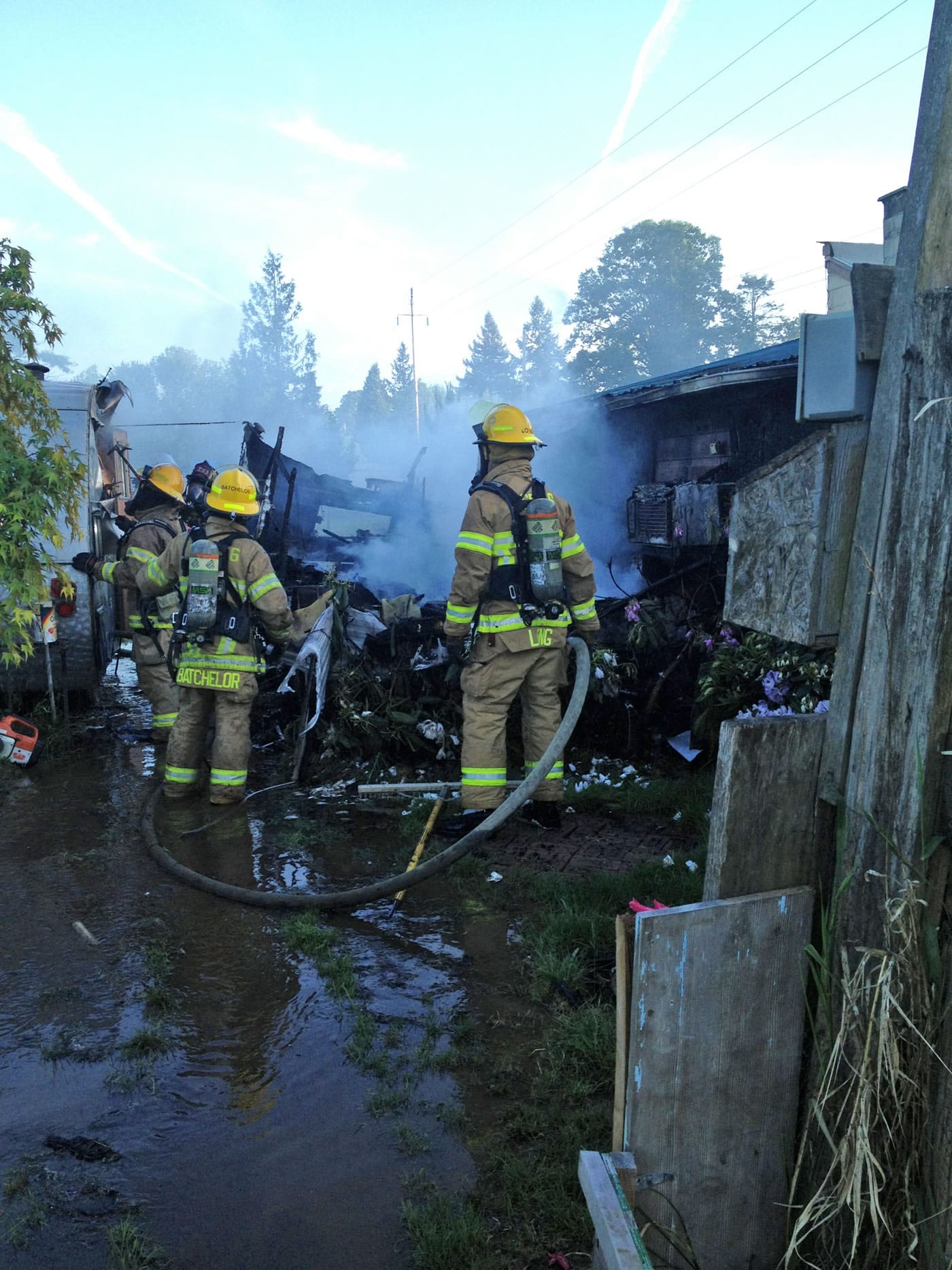 Firefighters mop up the scene of a fire in Ridgefield on Tuesday, where flames destroyed a camper trailer and threatened adjacent structures.