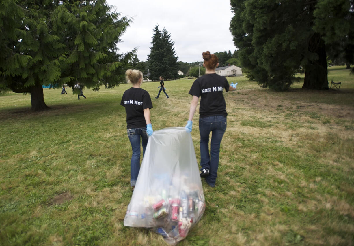 Woodland High School cheerleaders Justise Anderson, left, and Ally Baluta, 15, join a group of athletes helping to clean up the mess after the July 4th celebration at Fort Vancouver.