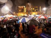 Crowds of people wearing raincoats and huddled under umbrellas attend the Vancouver Rotary Foundation's 17th annual community tree-lighting Friday evening at Esther Short Park.