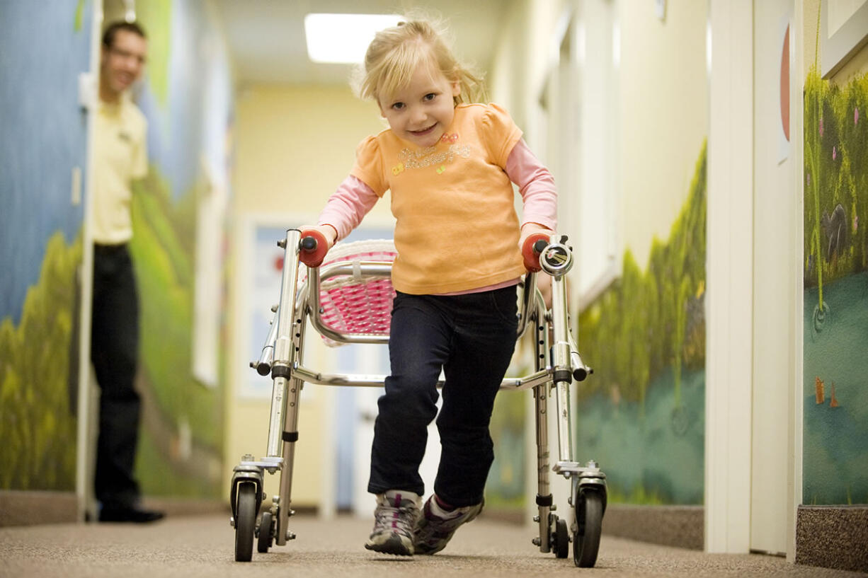 Katie Califf, 4 1/2 , with physical therapist intern Casey Berg watching, walks to a therapy session at the ARC Family Center in March 2011.