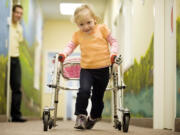 Katie Califf, 4 1/2 , with physical therapist intern Casey Berg watching, walks to a therapy session at the ARC Family Center in March 2011.