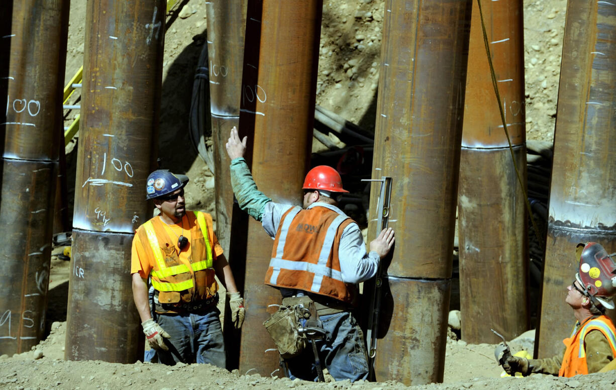 Workers at the site help drive metal piles 100 feet into the earth on Thursday to be part of a sturdy foundation for a new railroad bridge.