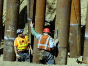 Workers at the site help drive metal piles 100 feet into the earth on Thursday to be part of a sturdy foundation for a new railroad bridge.