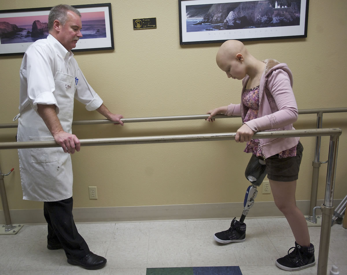 Caitlyn Lippolis, 12, takes her first steps with a prosthetic leg at Artisan Technologies in Tualatin, Ore., last month. Warren Mays, left, is president of Artisan Technologies, which constructed the leg.