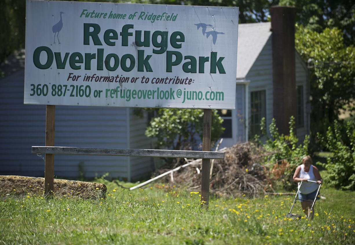 A woman cuts grass Wednesday near a sign at the property for the proposed Overlook Park in Ridgefield.