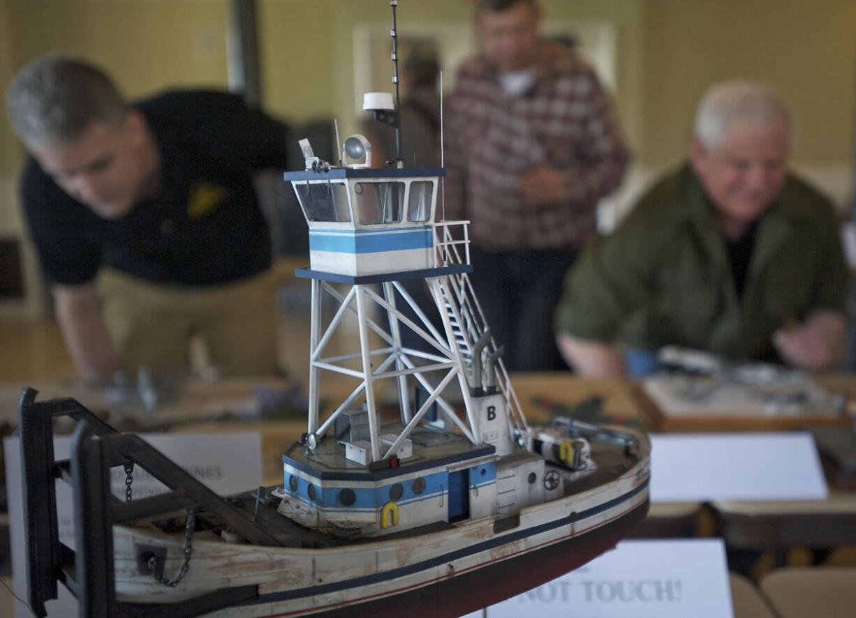 A model tug boat sits in the foreground as judges (background from left) Terry Werdel, Mark Peterson and Mike LaLone look over other entries during the IPMS LT.