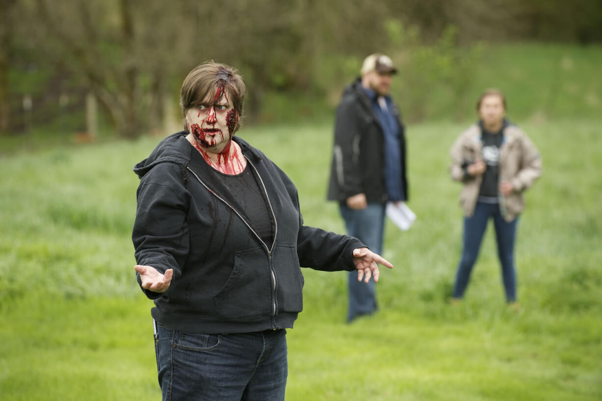 Columbian reporter Sue Vorenberg practices her moves as a slow &quot;Romero zombie&quot; during her day as an extra in director Nick Hagen's new zombie Web series &quot;Zombie Ridge.&quot; Hagen, center, and Sunshine, an actress from his &quot;The Haunting of Sunshine Girl&quot; YouTube series, right, discuss details in the background.