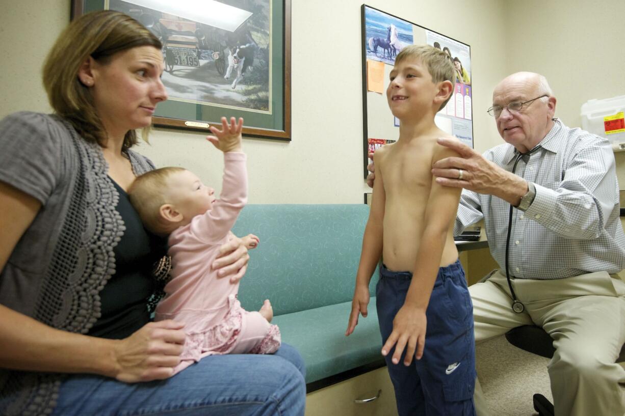 Dr. Gerry Bader, right, performs a physical exam on Jonah Bustad, 6, as Jonah's mother, Monica, 35, and sister, JennaLynn, 10 months, watch in an exam room at The Vancouver Clinic in Salmon Creek on Tuesday.