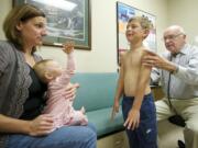 Dr. Gerry Bader, right, performs a physical exam on Jonah Bustad, 6, as Jonah's mother, Monica, 35, and sister, JennaLynn, 10 months, watch in an exam room at The Vancouver Clinic in Salmon Creek on Tuesday.