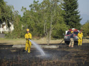 Firefighters water down the burned grass to prevent the fire from reigniting.