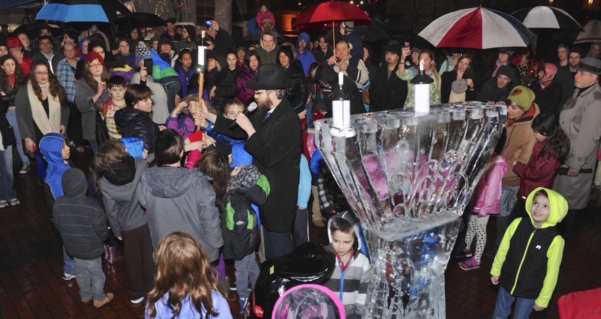 Chabad Jewish Center Rabbi Shmulik Greenberg, center, leads a group of children in a prayer next to an ice sculpture of a menorah at a Hanukkah celebration and menorah lighting Sunday in Esther Short Park in Vancouver.