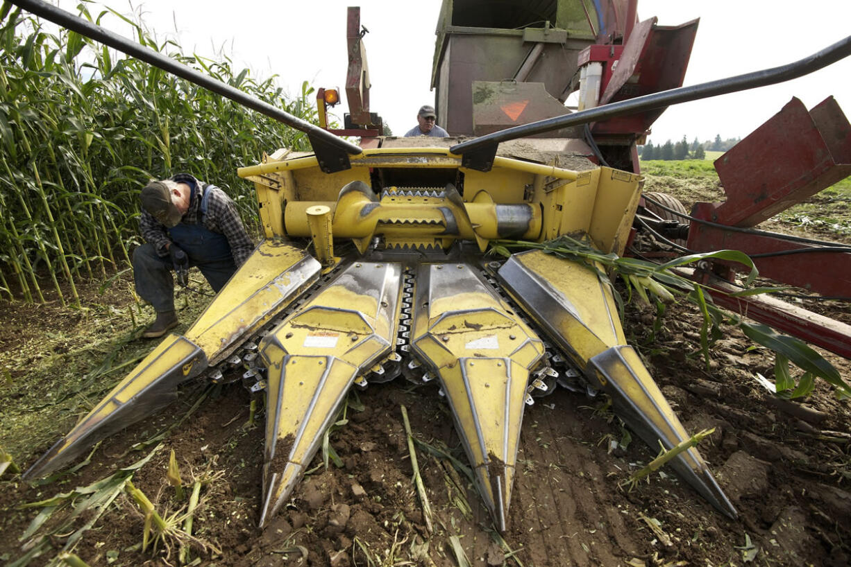 Jim Walker, left, and John Mettler Jr., background center, service equipment while harvesting corn Wednesday at a Ridgefield farm.