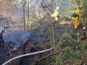 Firefighters hose down a forest fire that burned through nearly 2 acres Tuesday evening in north Clark County along the East Fork Lewis River.