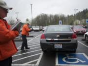 Parking enforcement volunteer Tom Croley, right, takes photos as his partner Gary Anderson writes out a ticket during a recent patrol in the Legacy Salmon Creek lot.